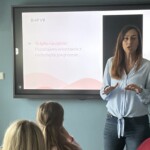 Trenerka prowadzi szkolenie. Za nią tablica z prezentowaną treścią zajęć.